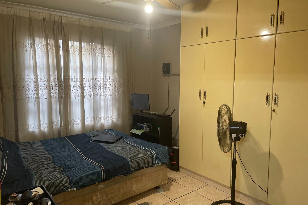 A bedroom featuring tiled flooring, a ceiling fan, and built-in cupboards providing ample storage space.