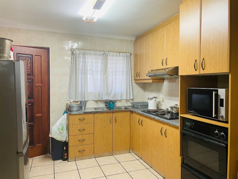 Functional kitchen featuring laminate cabinetry, built-in oven, electric hob, extractor fan, and tiled finishes throughout.