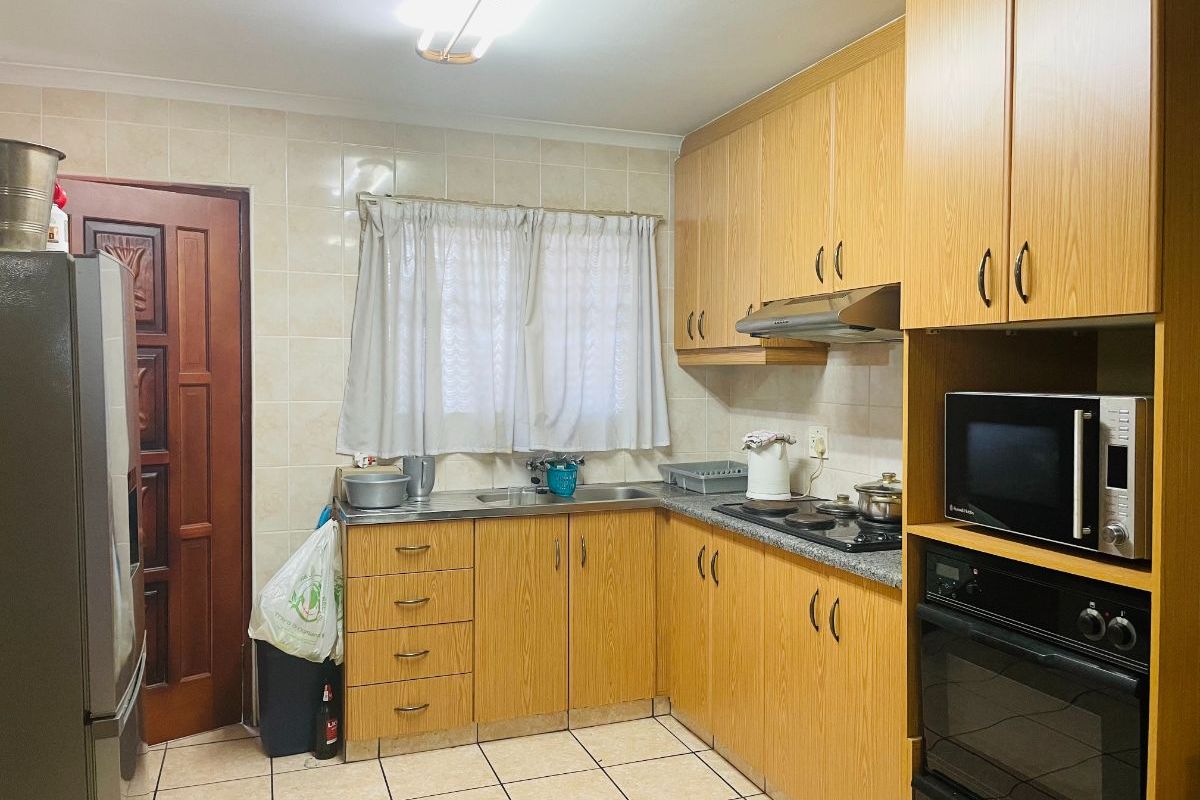 Functional kitchen featuring laminate cabinetry, built-in oven, electric hob, extractor fan, and tiled finishes throughout.
