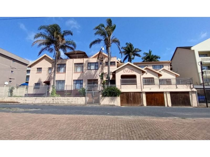 Front elevation of the Cycad apartment complex, featuring a gated entrance, perimeter fencing, and multiple garage doors at street level.