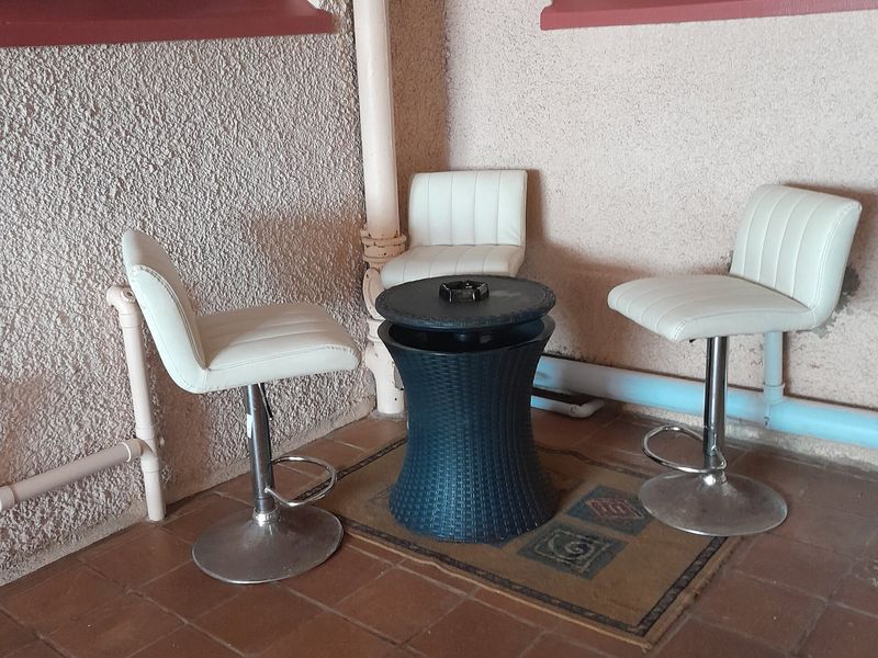 A small outdoor patio area featuring tiled flooring and security-barred windows, showing signs of wear on the exterior wall finishes.