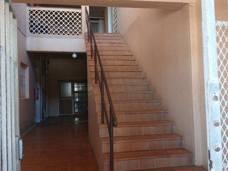 An exterior entrance area featuring a tiled staircase with a metal handrail and security gate access to the apartment building.