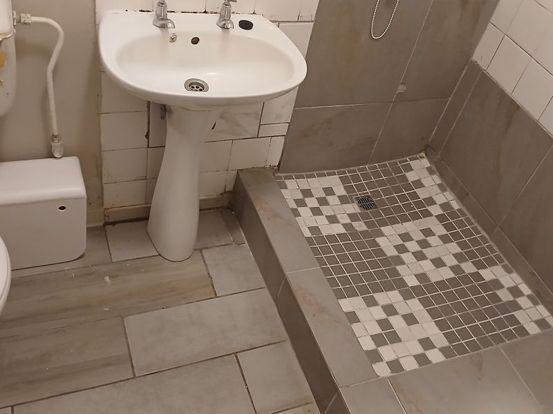 A functional bathroom featuring a pedestal basin, toilet, and a tiled shower area. The space requires cosmetic updates and maintenance to improve its condition.