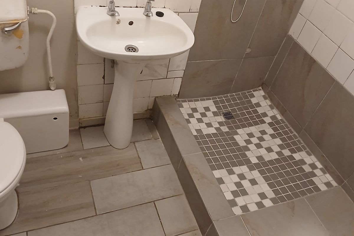 A functional bathroom featuring a pedestal basin, toilet, and a tiled shower area. The space requires cosmetic updates and maintenance to improve its condition.