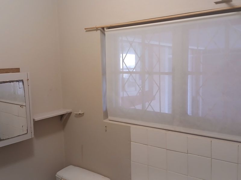A functional bathroom space featuring a wall-mounted medicine cabinet, tiled splashback, and a window fitted with security bars and a roller blind.