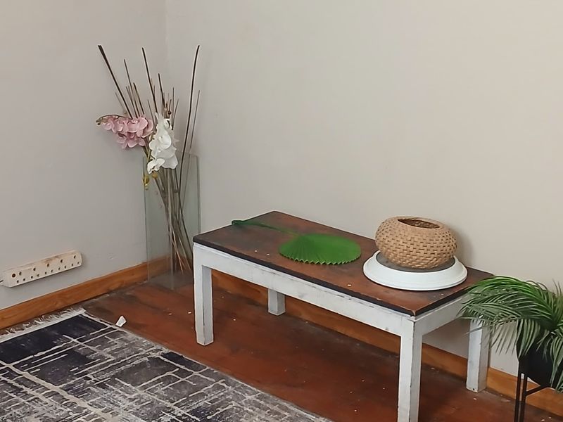 A corner view of a living area featuring wooden flooring, neutral wall paint, and standard electrical fixtures.