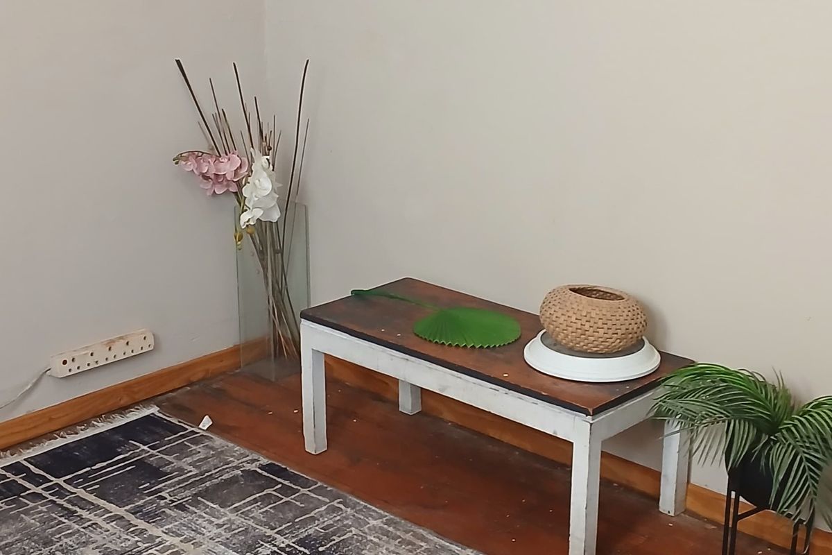 A corner view of a living area featuring wooden flooring, neutral wall paint, and standard electrical fixtures.