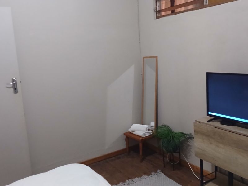 A simple bedroom featuring wooden flooring and a high-level window, providing a functional and neutral space.