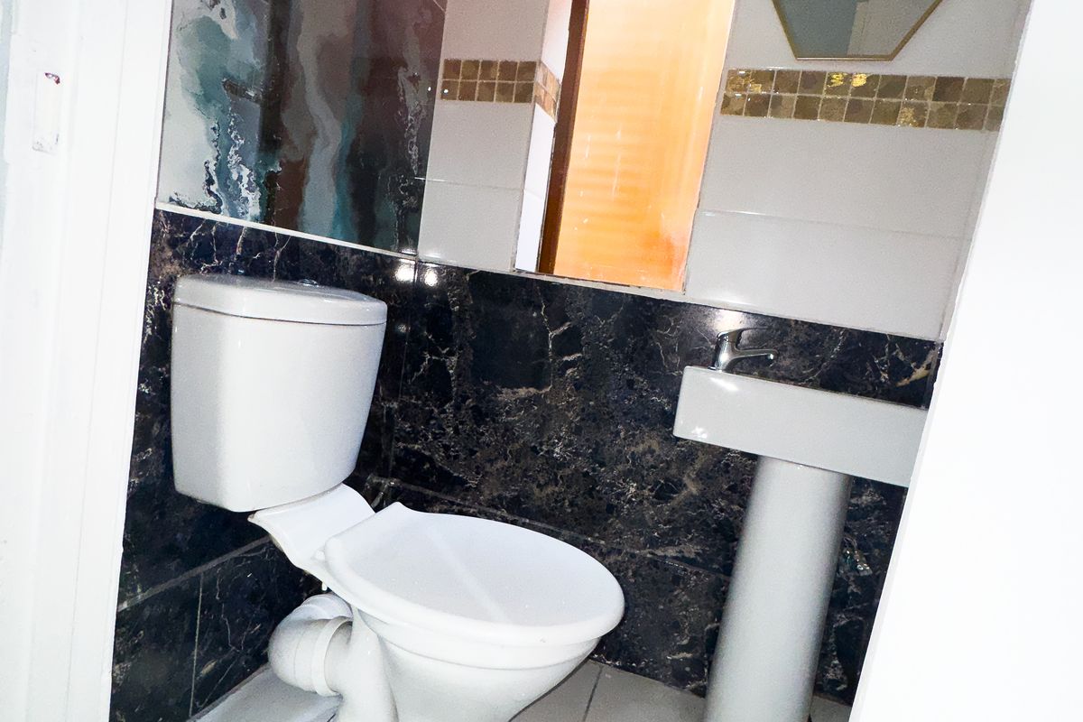 A compact bathroom featuring a pedestal sink, toilet, and contrasting dark marble-effect wall tiling with decorative accents.