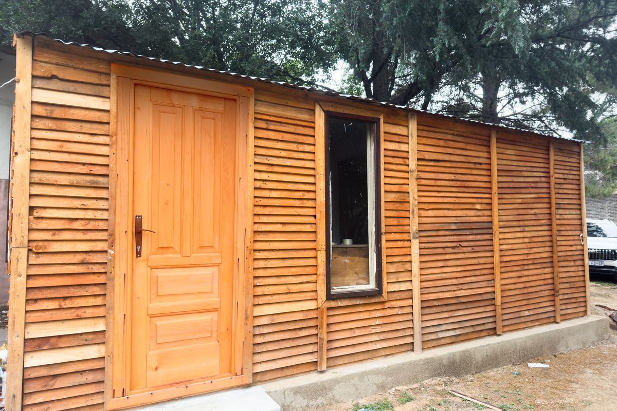 Exterior view of a timber-clad structure featuring a wooden door and a single window, set on a concrete foundation.