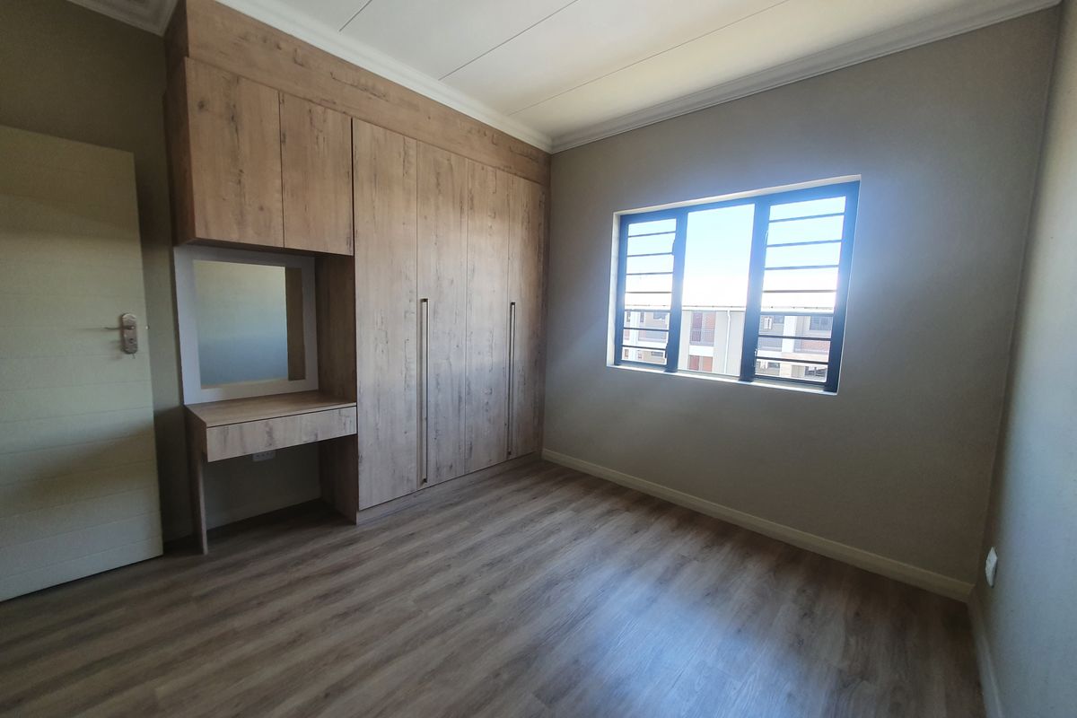 A bright bedroom featuring modern wood-look laminate flooring, built-in cabinetry with an integrated vanity, and security bars on the window.