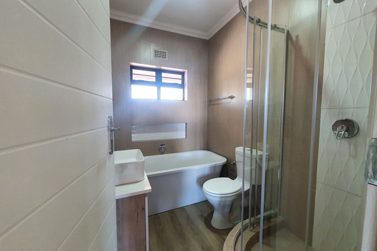 A modern bathroom featuring a bathtub, a separate glass-enclosed shower, a vanity with a vessel sink, and neutral wall tiling.