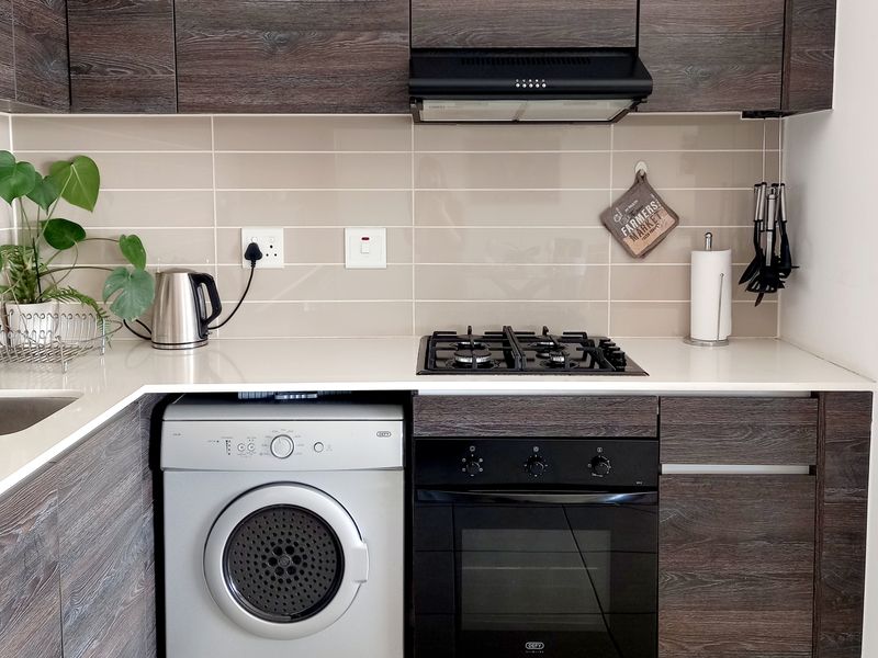 Modern kitchen featuring dark wood grain cabinetry, stone countertops, a gas hob, built-in oven, extractor fan, and integrated laundry plumbing.
