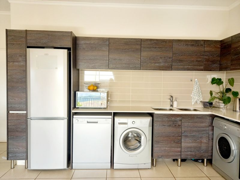 Modern kitchen featuring dark wood-grain cabinetry, tiled backsplash, double sink, and integrated space for multiple appliances including a dishwasher and washing machine.