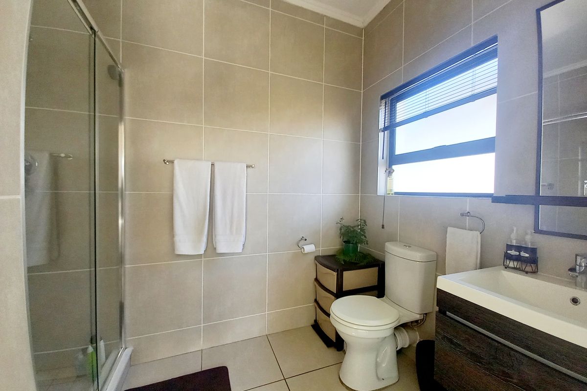 A well-maintained bathroom featuring a glass shower enclosure, modern vanity with integrated basin, neutral wall and floor tiling, and a window for natural light.