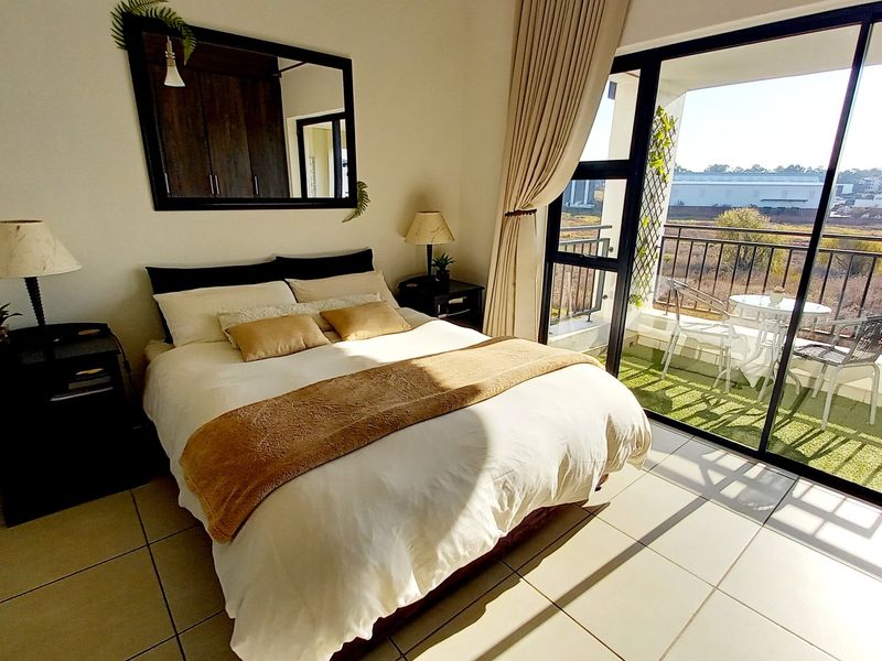 A bright bedroom featuring tiled flooring, built-in cupboards, and a large sliding glass door providing direct access to a private balcony.