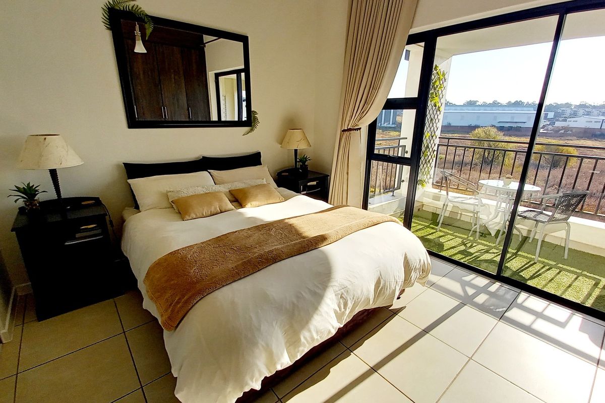 A bright bedroom featuring tiled flooring, built-in cupboards, and a large sliding glass door providing direct access to a private balcony.