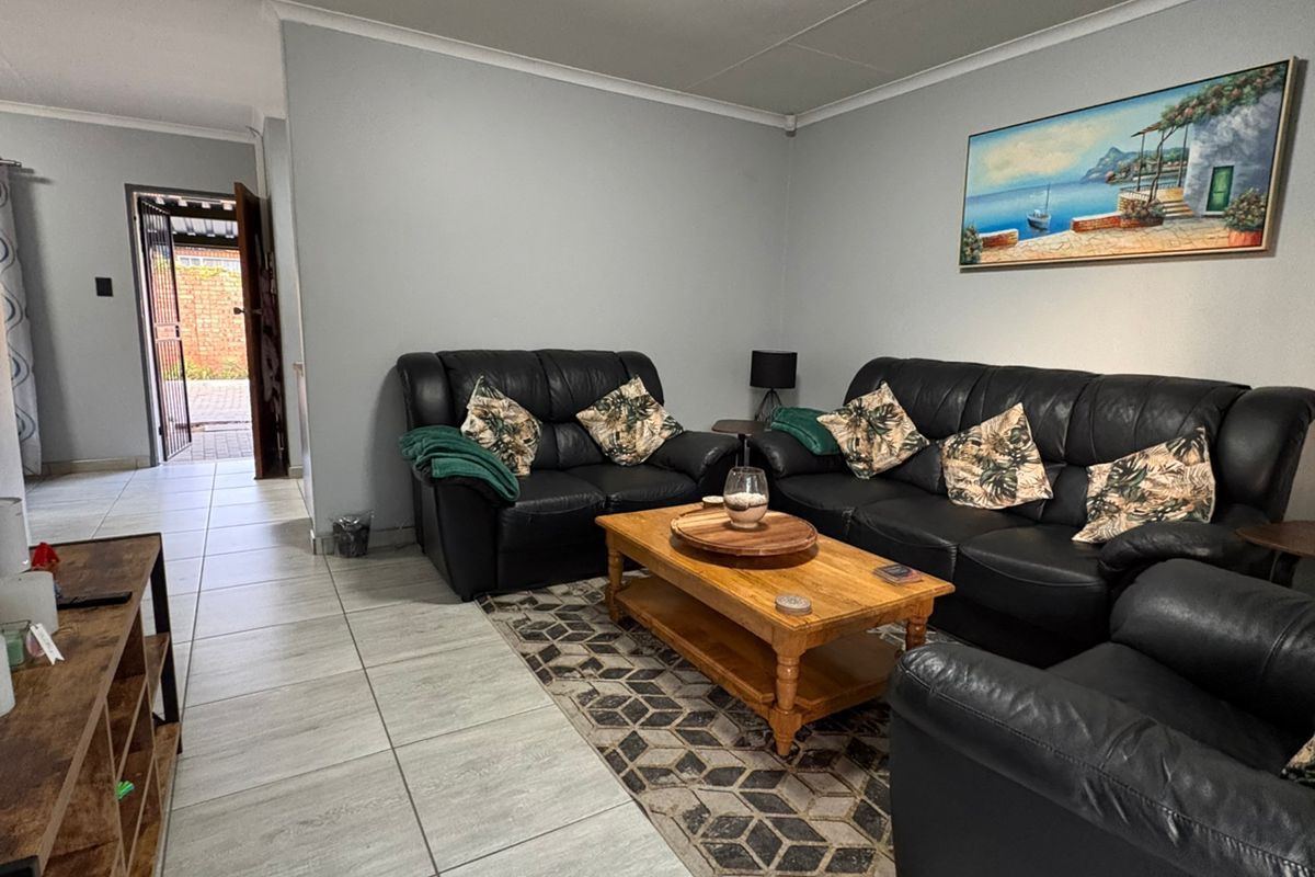 A well-lit living room featuring neutral tiled flooring, leading towards an exterior entrance door.