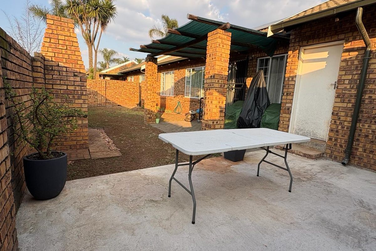 A private rear courtyard featuring a concrete patio, brick boundary walls, and a covered pergola area, offering potential for outdoor living and landscaping.