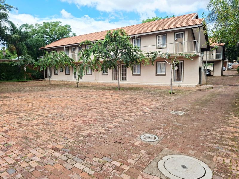Exterior view of a multi-story apartment complex featuring a large brick-paved courtyard, tiled roofing, and balcony access with security gates.
