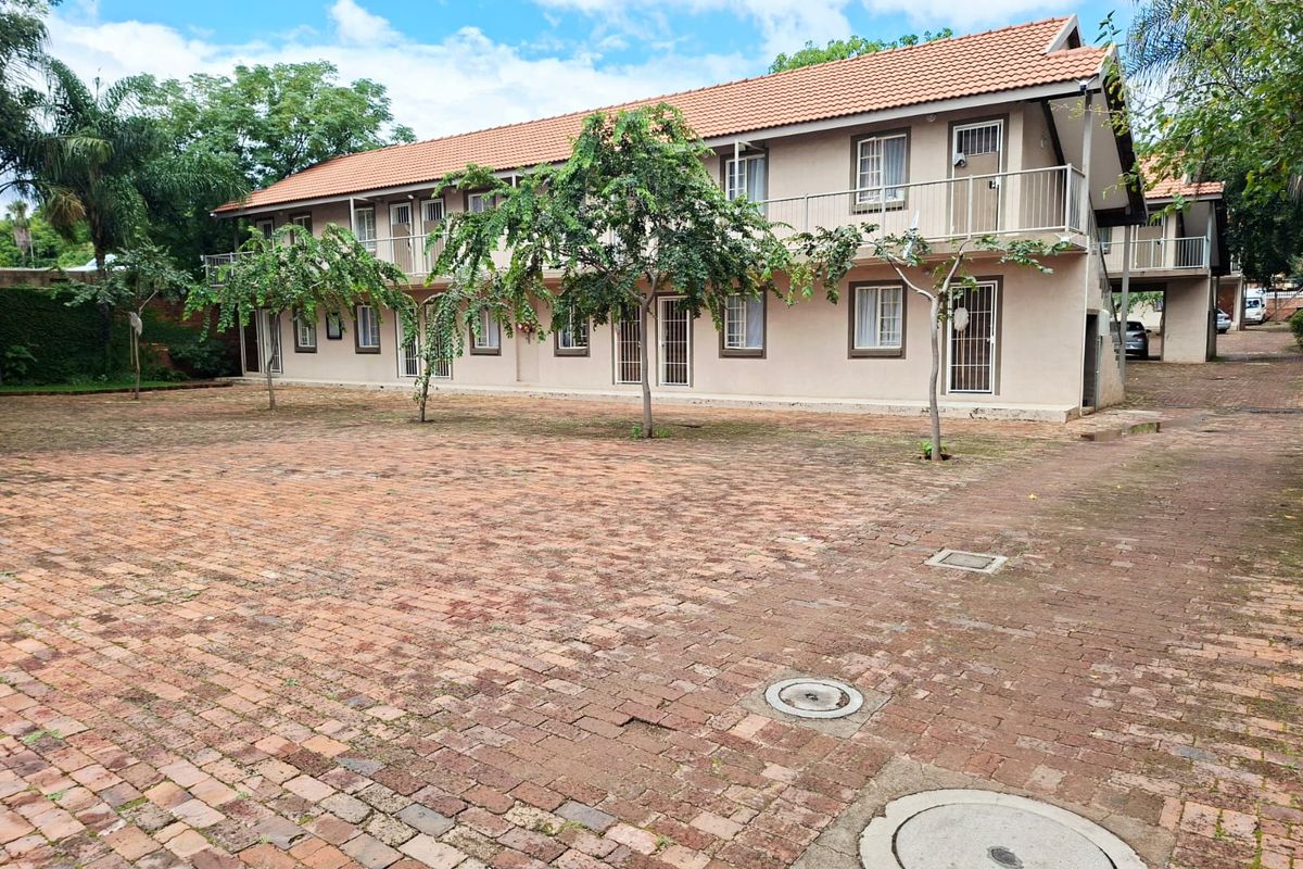 Exterior view of a multi-story apartment complex featuring a large brick-paved courtyard, tiled roofing, and balcony access with security gates.