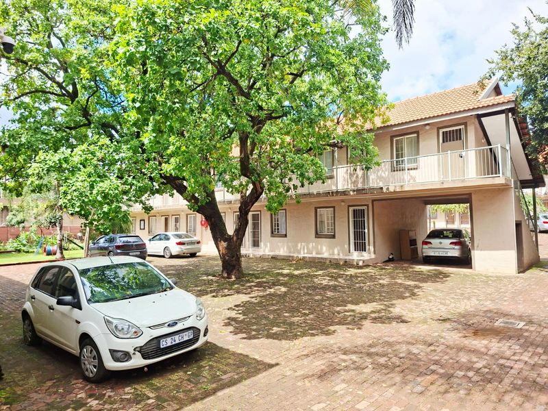 Exterior view of an apartment complex featuring brick paving, covered parking bays, and upper-level balconies with security gates.