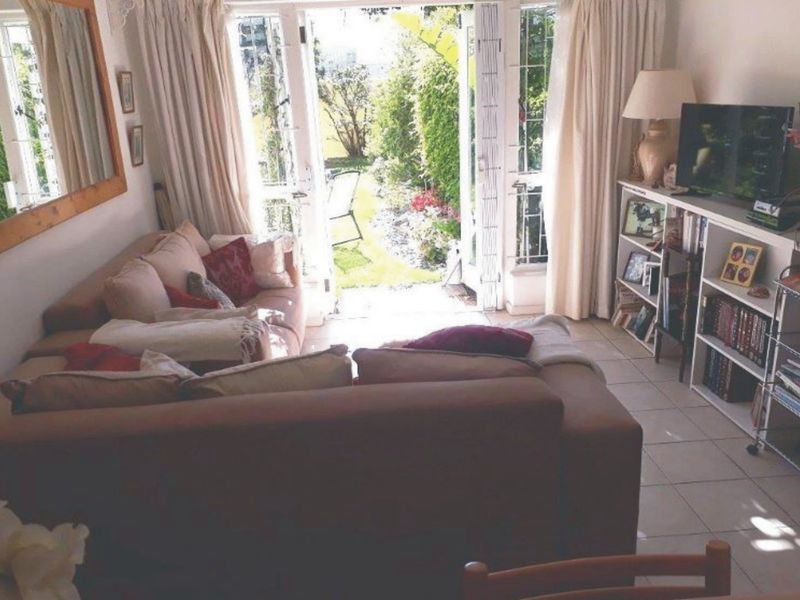 A comfortable living room featuring tiled flooring and double french doors that open directly onto a private garden area.