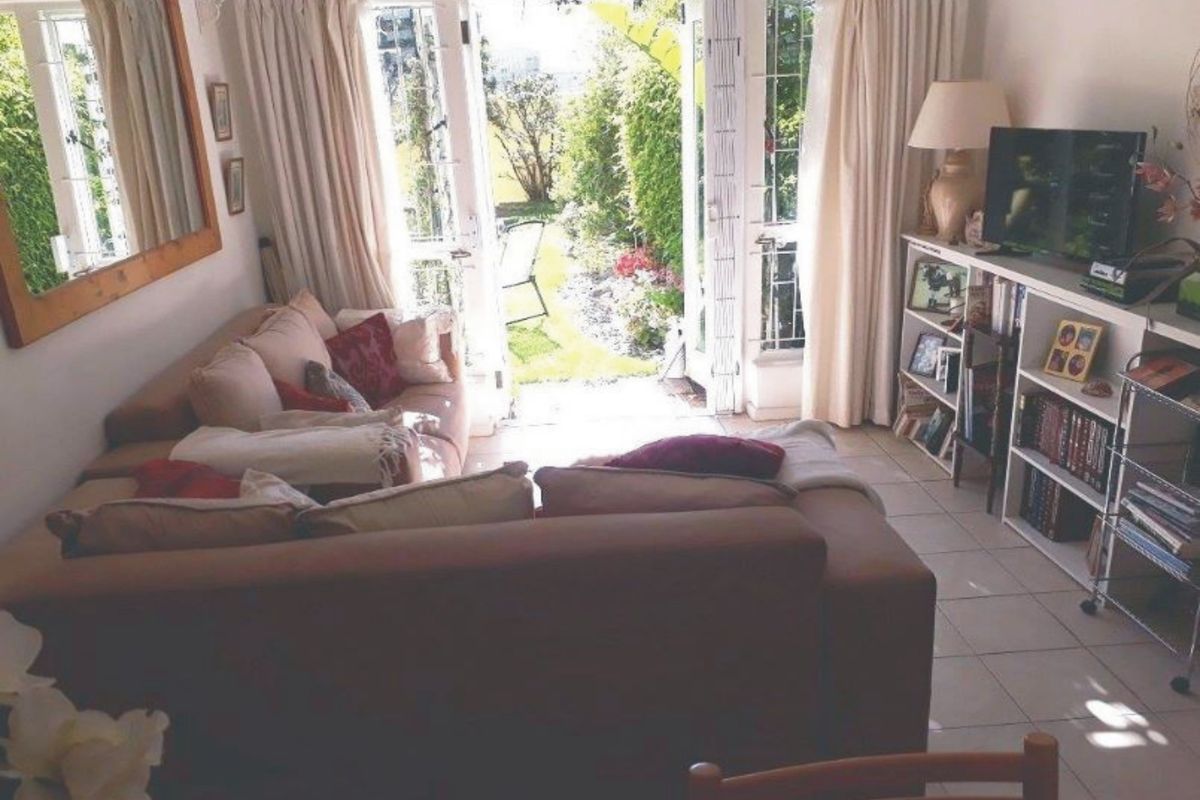 A comfortable living room featuring tiled flooring and double french doors that open directly onto a private garden area.