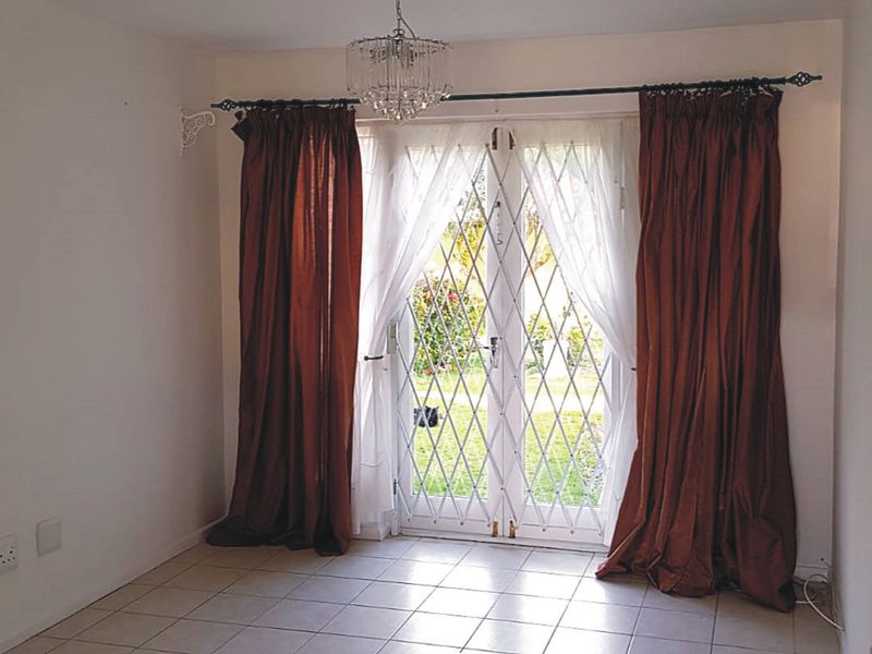 An empty living room featuring tiled flooring and double glass doors with a security gate, providing direct access to the outdoor area.