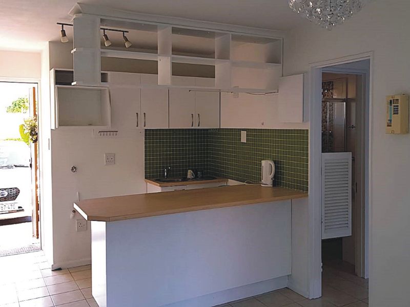 A compact kitchen featuring white cabinetry, a green tiled backsplash, and a breakfast bar, with direct access to an exterior entrance.