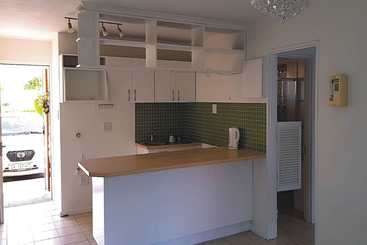 A compact kitchen featuring white cabinetry, a green tiled backsplash, and a breakfast bar, with direct access to an exterior entrance.