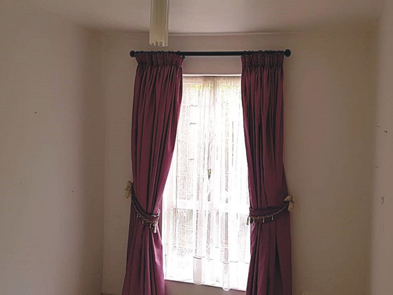 A vacant bedroom featuring a window with a curtain rod, requiring minor wall repairs and cosmetic updates.
