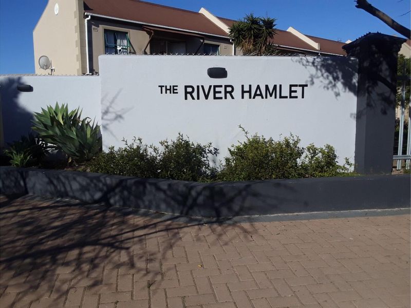 Entrance view of The River Hamlet apartment complex, featuring a paved driveway and a well-maintained boundary wall with signage.