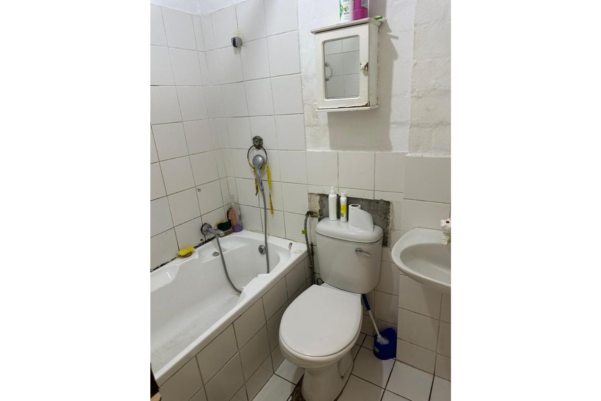 A dated bathroom featuring a bathtub, toilet, and wall-mounted basin, requiring significant renovation and repair to the wall finishes and tiling.