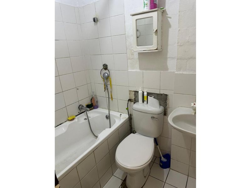 A dated bathroom featuring a bathtub, toilet, and wall-mounted basin, requiring significant renovation and repair to the wall finishes and tiling.