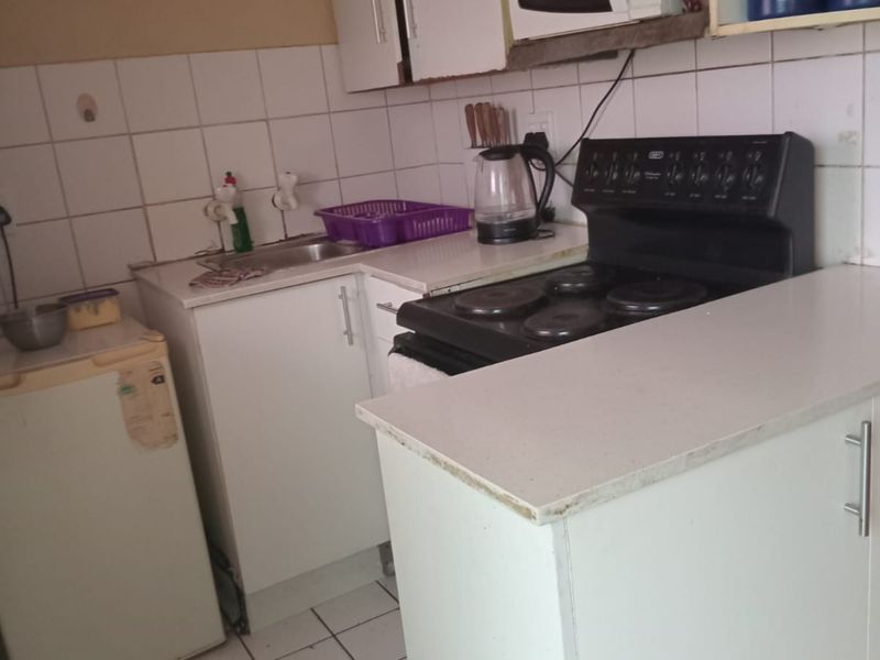 Compact kitchen featuring white cabinetry, tiled backsplash, electric stove, and tiled flooring. The space requires cosmetic updates to improve its overall condition.
