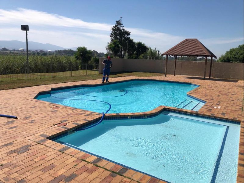Outdoor pool area featuring a paved deck, a gazebo, and a perimeter fence with views of the surrounding landscape.