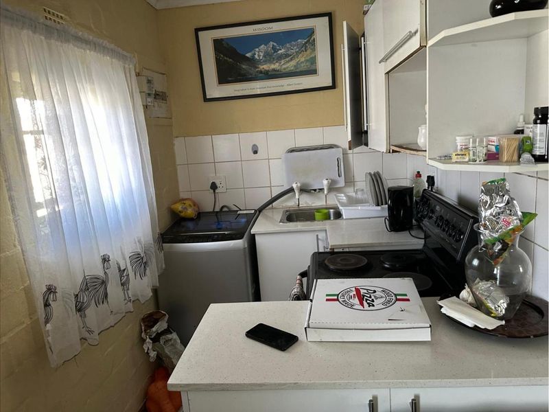 A compact kitchen featuring built-in cabinetry, a sink, and an electric stove, requiring cosmetic updates to improve its overall aesthetic and functionality.