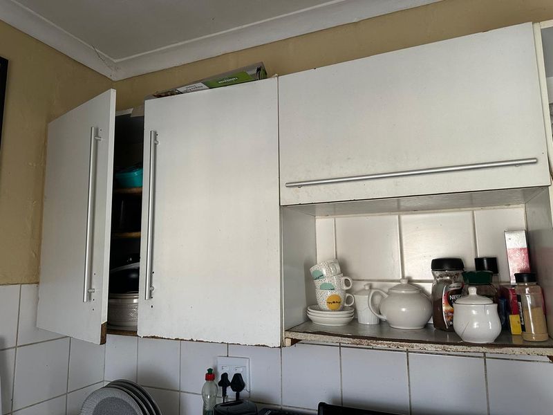 Close-up view of kitchen wall cabinetry featuring white laminate doors, tiled splashback, and visible wear on the cabinet edges.
