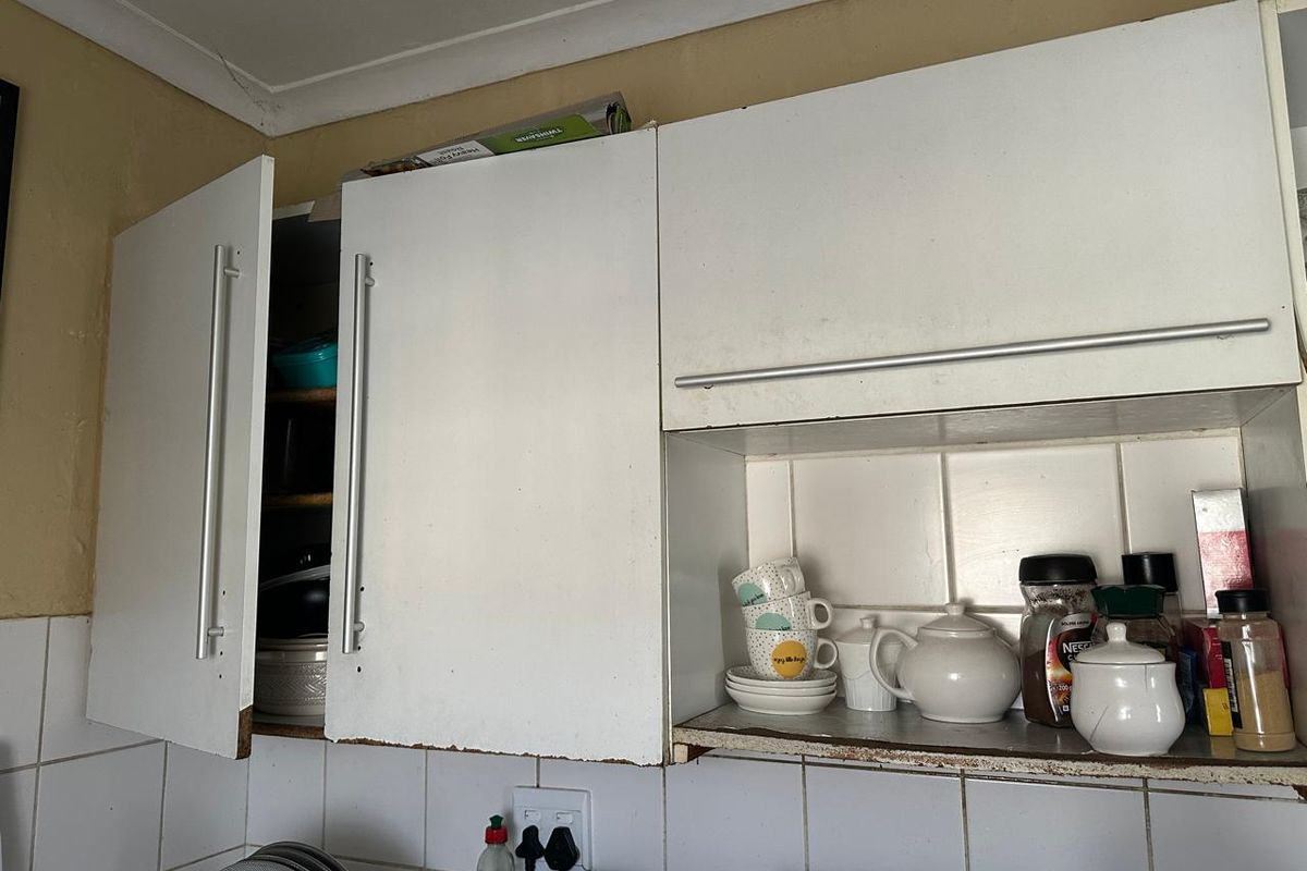 Close-up view of kitchen wall cabinetry featuring white laminate doors, tiled splashback, and visible wear on the cabinet edges.