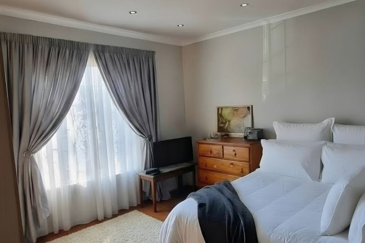 A well-lit bedroom featuring hardwood flooring, recessed ceiling lighting, and large windows with curtains, creating a comfortable and inviting living space.