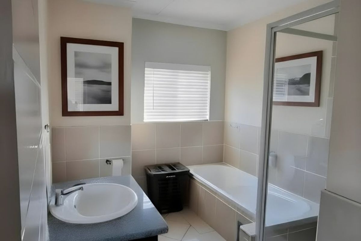 A functional bathroom featuring a vanity with a basin, a built-in bathtub, and a separate glass-enclosed shower stall with neutral wall tiling.