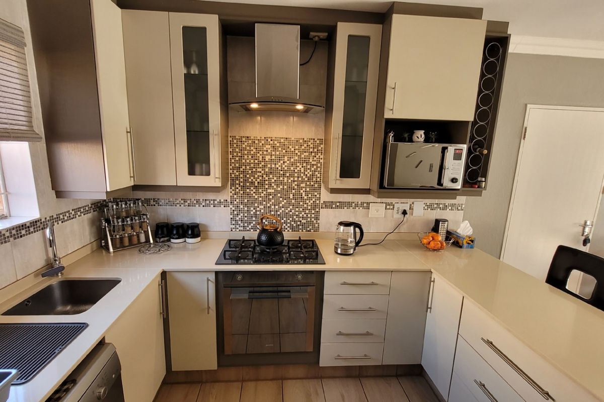 Modern kitchen featuring stone countertops, gas hob, built-in oven, stainless steel extractor fan, and ample cabinetry with a dedicated wine rack.