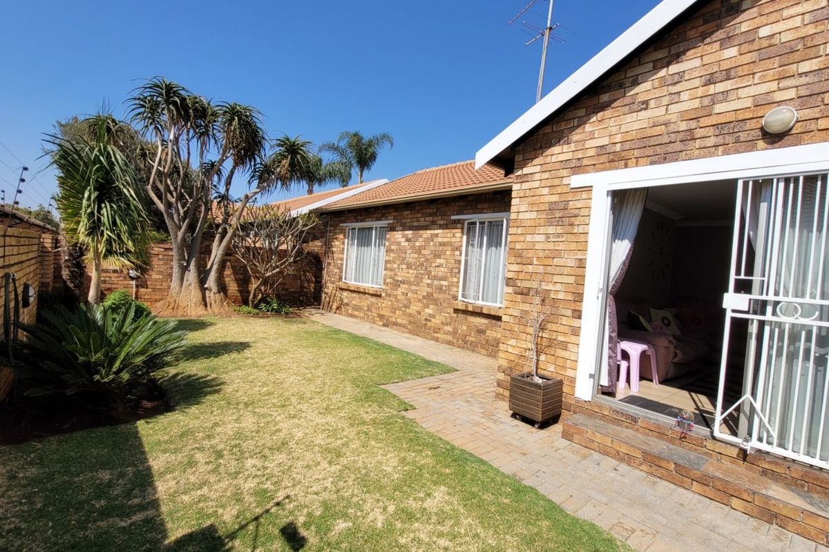 A well-maintained rear exterior view of a face brick townhouse featuring a private garden, paved walkway, and secure sliding door access.