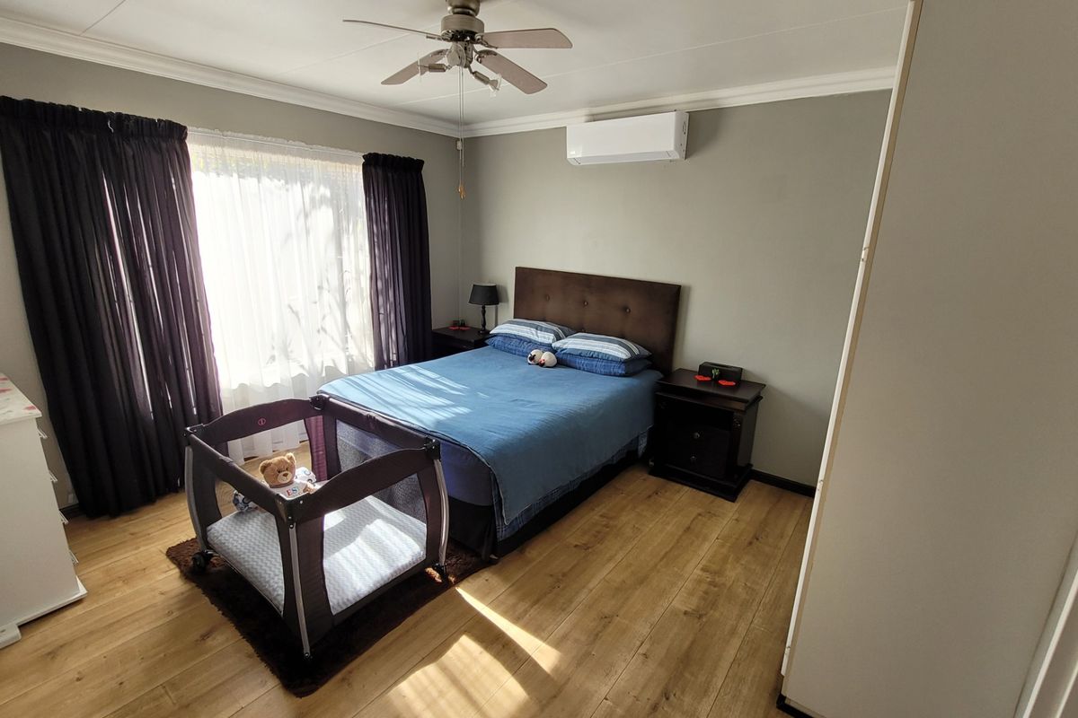 A well-maintained bedroom featuring laminate flooring, a ceiling fan, and a wall-mounted split-system air conditioner.