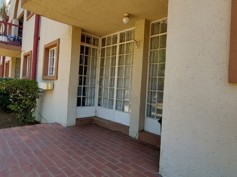 A covered ground-floor patio featuring brick paving and multiple glass-paned french doors providing access to the apartment interior.