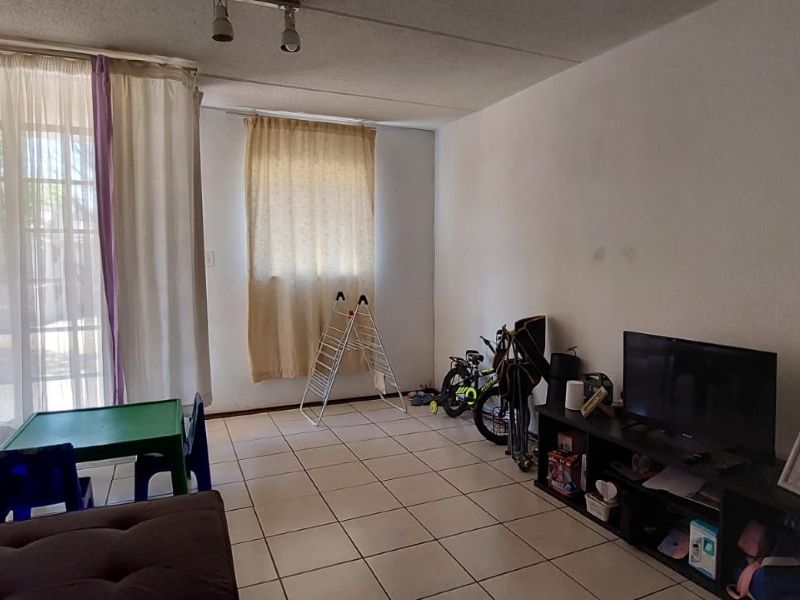 A living room featuring tiled flooring and a sliding glass door providing natural light. The space requires cosmetic updates to the wall finishes.