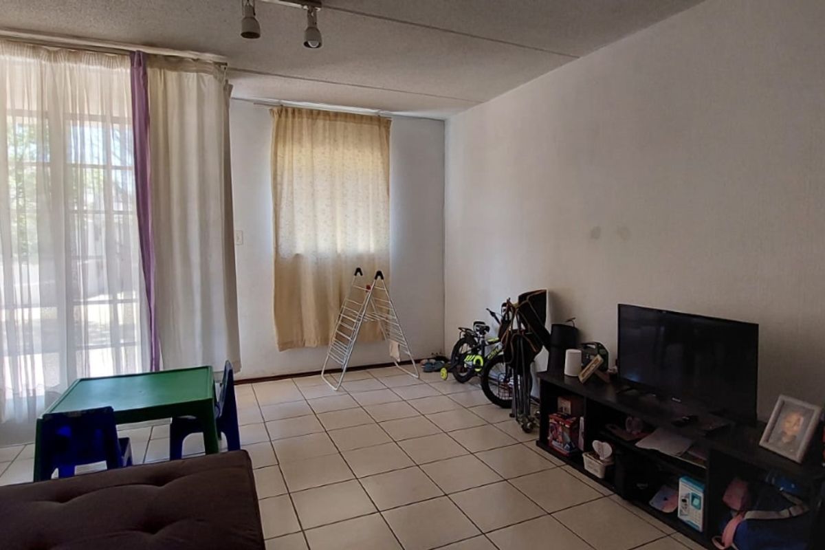 A living room featuring tiled flooring and a sliding glass door providing natural light. The space requires cosmetic updates to the wall finishes.