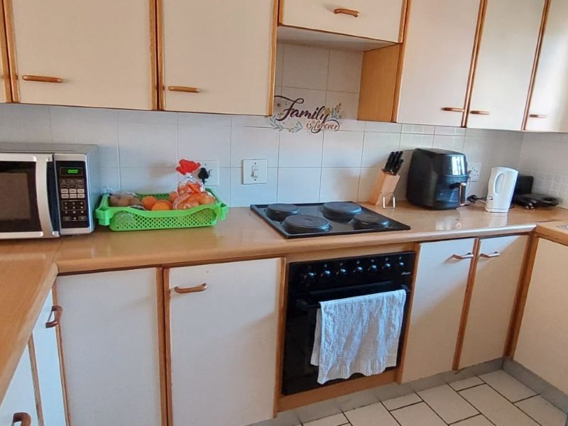 A functional kitchen featuring laminate countertops, built-in cabinetry, an electric hob, and an integrated oven with a tiled backsplash and floor.