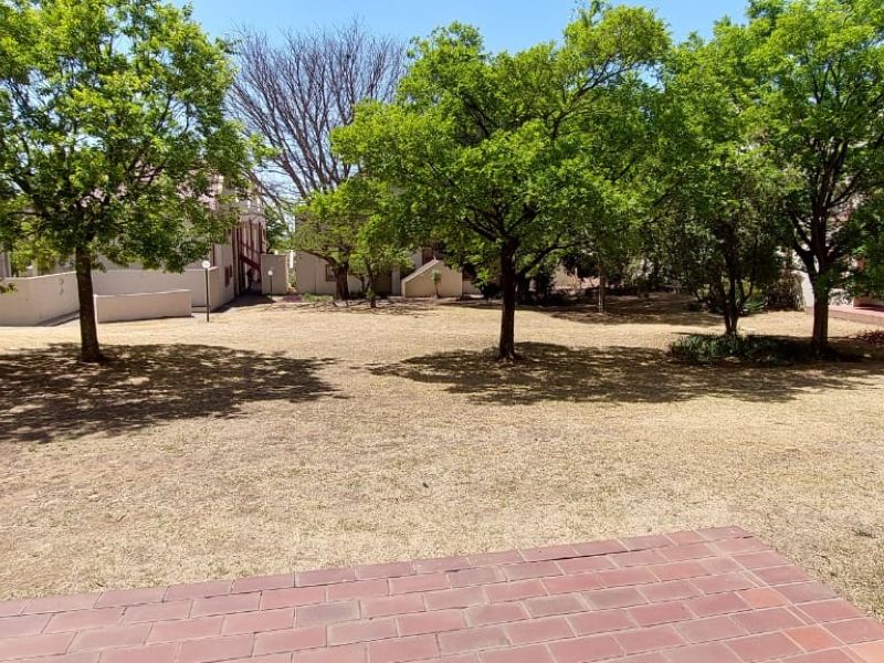 A spacious communal garden area featuring mature trees and a brick-paved patio space, offering a quiet outdoor setting within the apartment complex.
